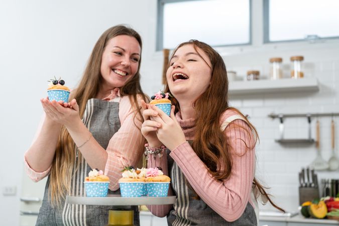 Daughter laughing with mother at home with cupcakes