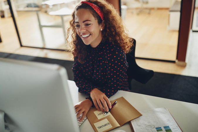 Woman with curly hair smiling at her computer with notes at work