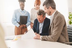 Two businessman checking contract at desk in a modern office, with two female colleagues