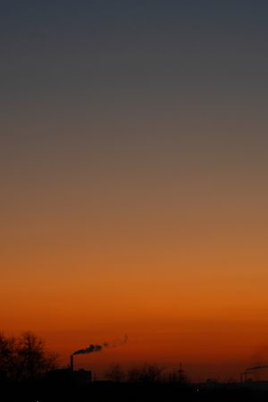 Orange gradient sky above silhouetted factory releasing smoky fumes