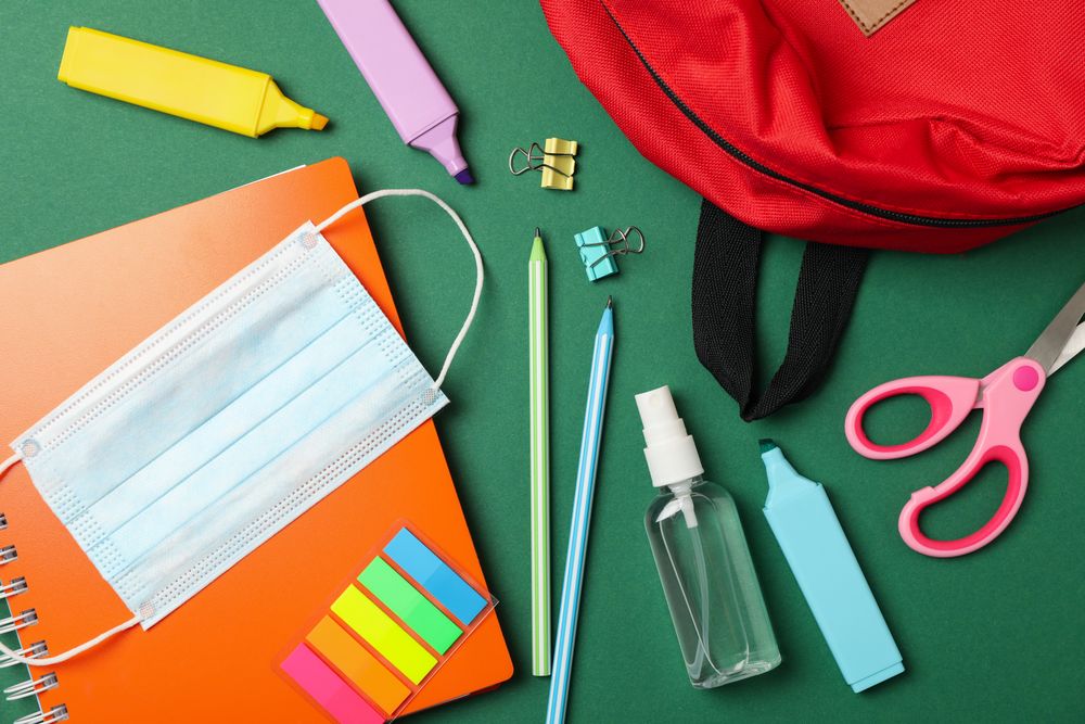School supplies with medical mask and sanitizer on green background