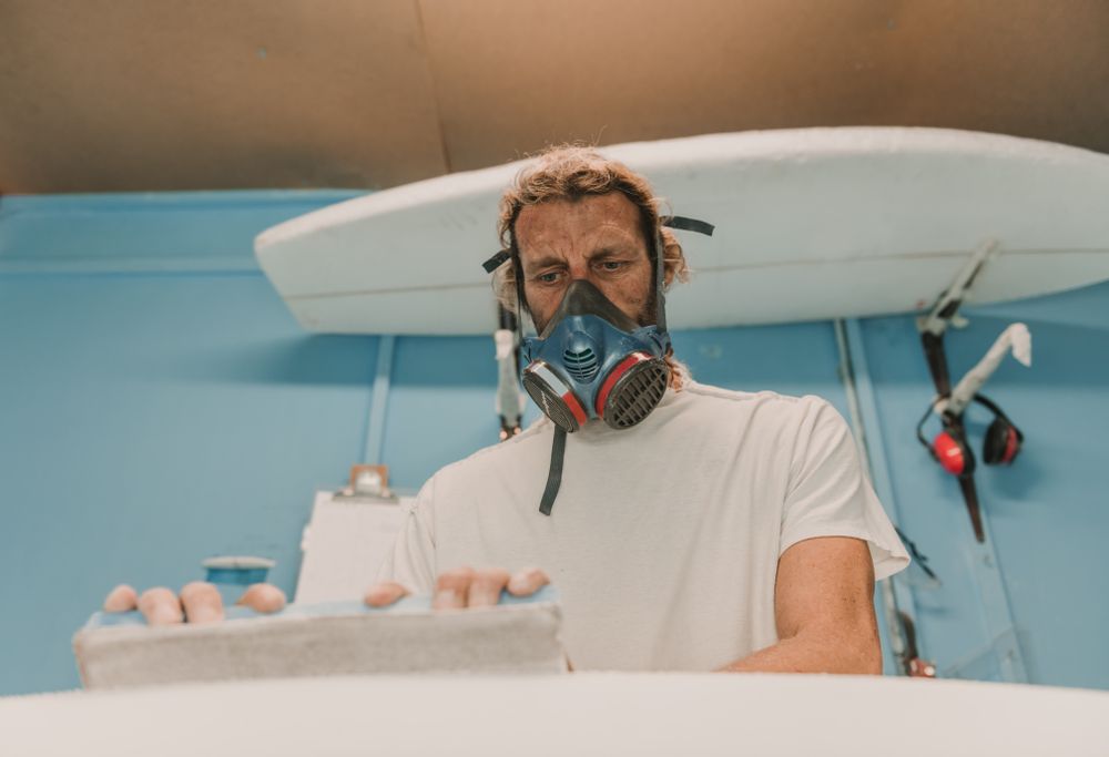 Man in respirator measuring surf board in workshop