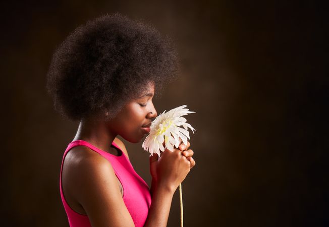 young woman with afro hair smelling a daisy with her eyes closed