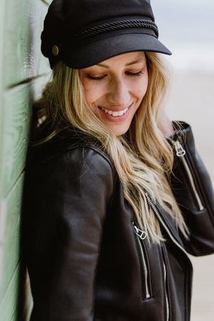 Stylish woman smiling and leaning on bright wooden cabins on beach