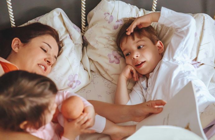 Closeup of mother reading story book to her kids lying in bed