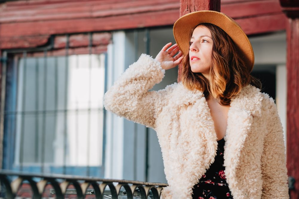 Smiling woman in warm wear standing near building and fence