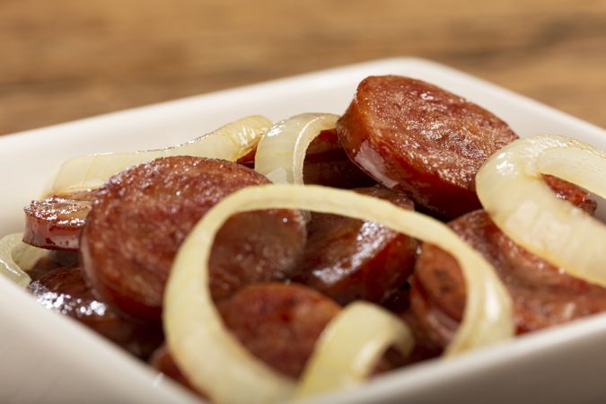 Sliced calabrese sausage with onion on wooden background.