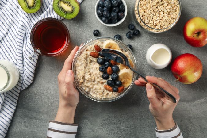 Woman eats oatmeal porridge. Composition with oatmeal on gray background