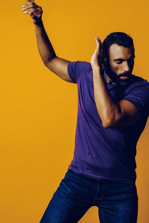 Black man in yellow studio with arms up to his side in protection, vertical composition