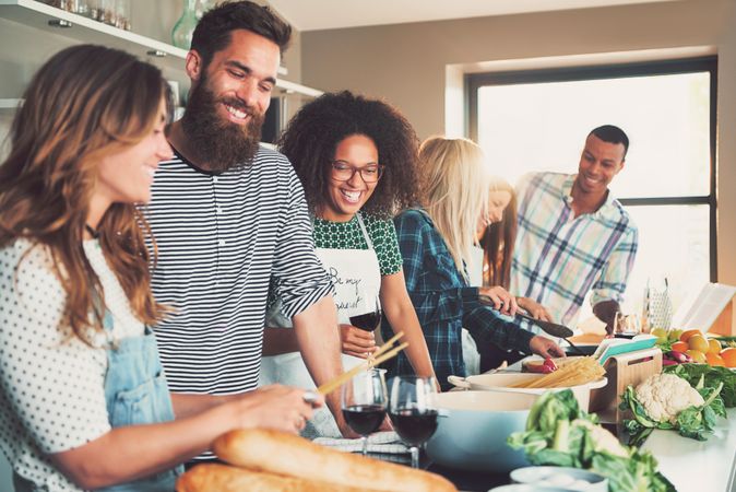 Happy friends drinking red wine and cooking pasta in a bright kitchen