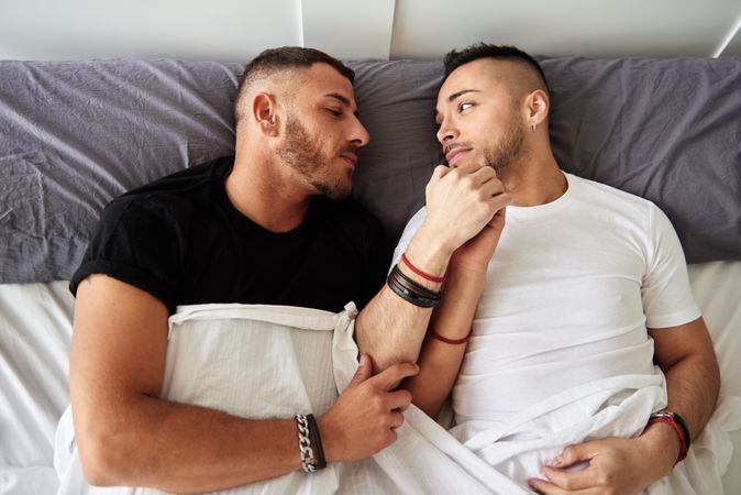 Smiling gay couple hugging on bed