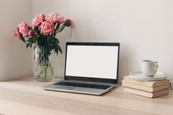 Glass vase with pink peonies bouquet, books and cup of coffee on wooden table