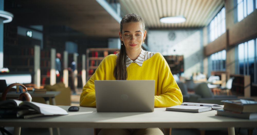 Thoughtful Multiethnic College Student Using Laptop Computer to Study in a Public Library. Young Woman Learning Online, Getting Ready for Exams, Browsing Internet to Prepare for Class