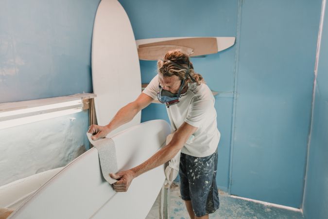 Man in respirator measuring surf board in workshop
