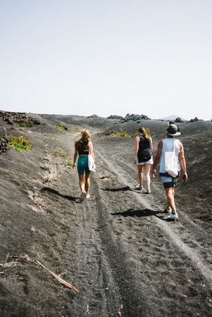 Three friends walking on dark sand trail in Lanzarote