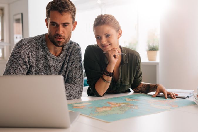 Young man and woman looking at laptop computer with world map in front