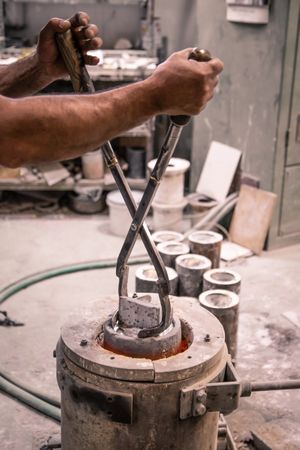Man with lifting tongs taking metal ware from crucible