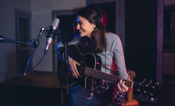 Female guitarist sitting in front of microphone and smiling in recording studio