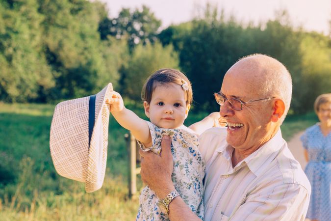 Baby girl playing with hat of older male outdoors