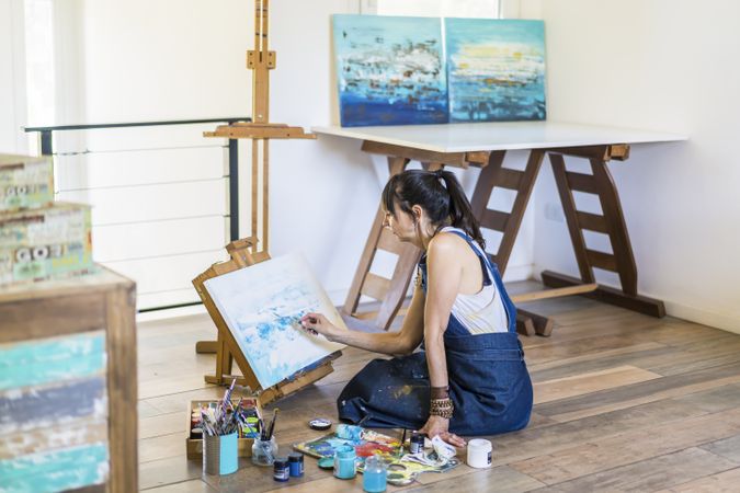 Woman artist painting on a canvas a blue abstract painting. Creative ywoman working on the floor in her art studio.