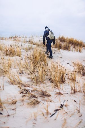 Man walking between sand field with dry grass