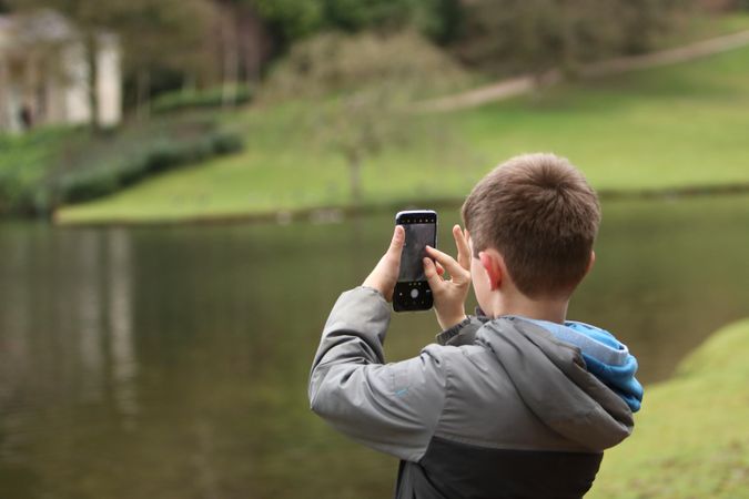 Boy taking a photo with smartphone beside lake