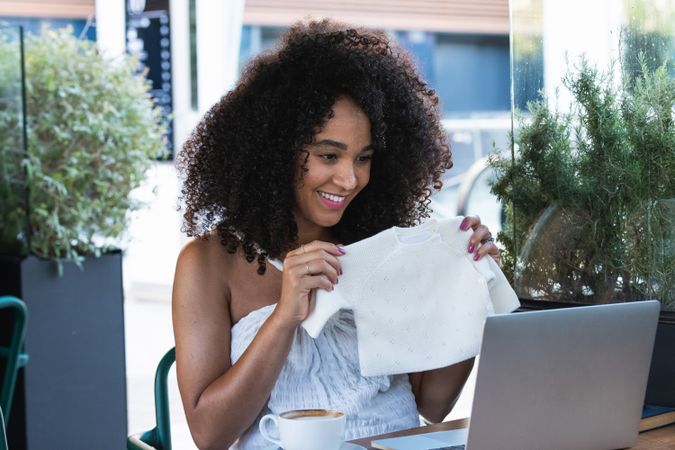 Smiling pregnant Black woman showing baby booties to laptop