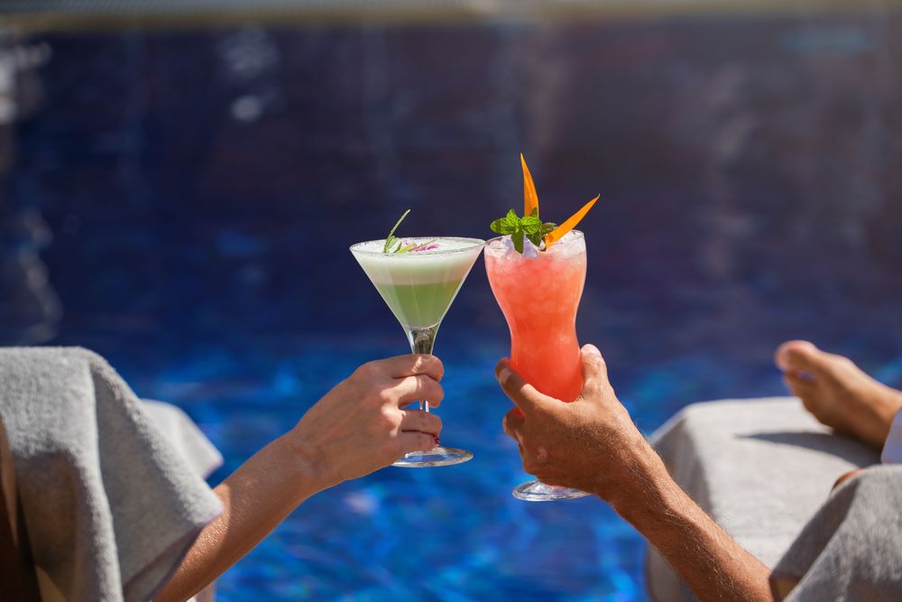 Crop woman and man clinking glasses of cocktails in poolside