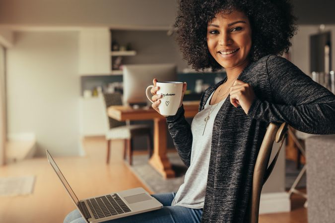 Portrait of young woman sitting at home with laptop and having coffee