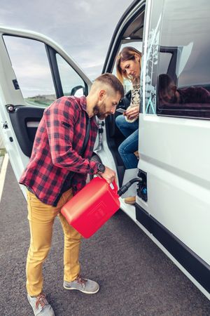 Male in red checkered shirt filling up van with gas can, vertical