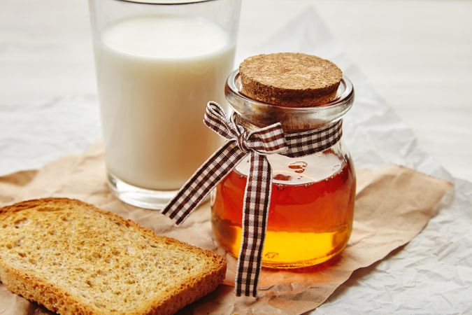 Closeup of honey jar with pretty ribbon as a gift with milk and toast