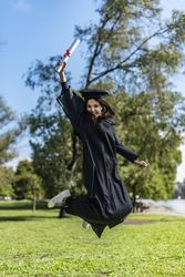 Happy graduating woman in a gown jumping while holding her diploma