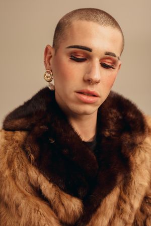 Close-up of man wearing makeup, earring and fur coat