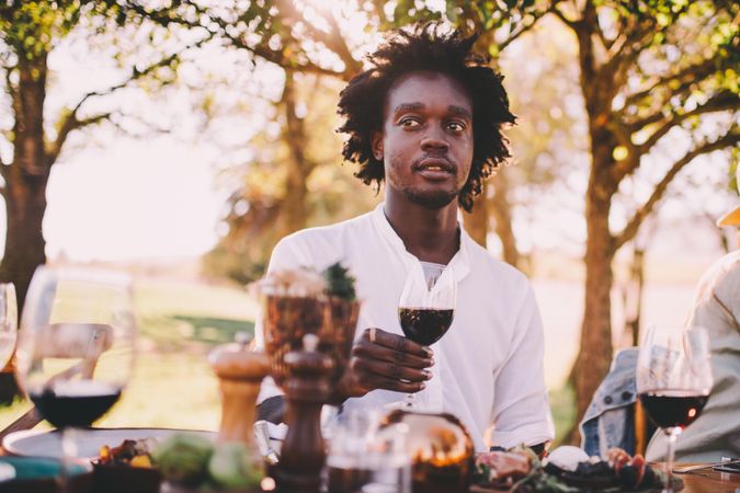 Man holding a glass of wine sitting at an outdoor table setting
