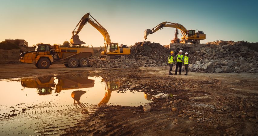 Aerial Drone Shot Of Construction Site With Heavy Machinery On Sunny Day: Diverse Team of Real Estate Developers Discussing Project. Engineer, Architect, Urban Planner Talking And Using Tablet.