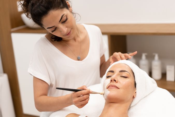 Female with towel on head having a relaxing face mask applied at beauty spa