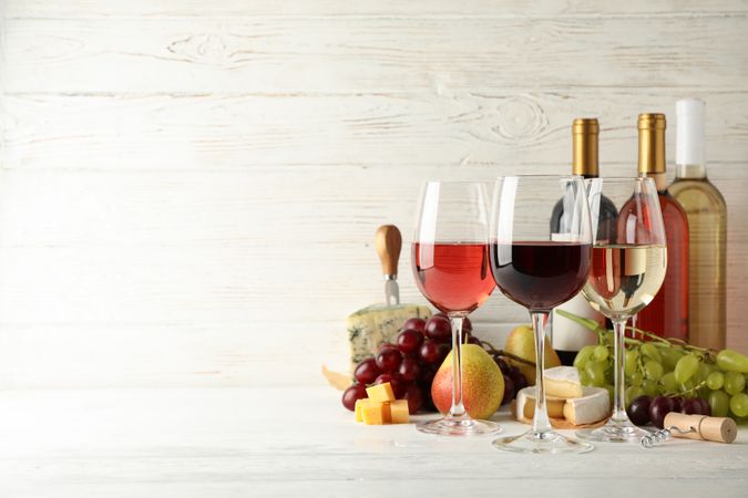 Fruits, cheese, bottles and glasses with different wine on light background, space for text