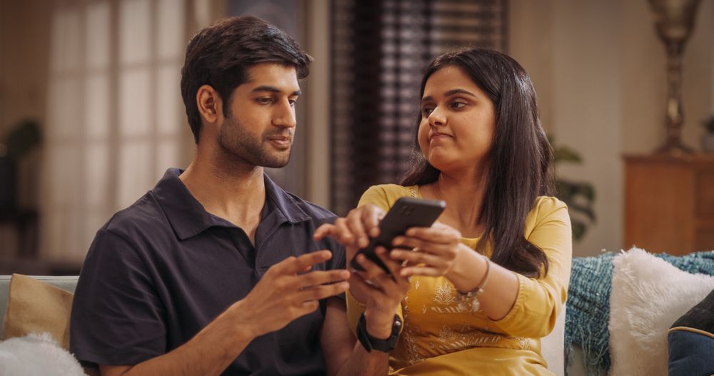 Young Indian Couple Sitting On The Sofa at Home: Woman Annoyed at her Boyfriend for Spending Too Much Time Online on Smartphone.