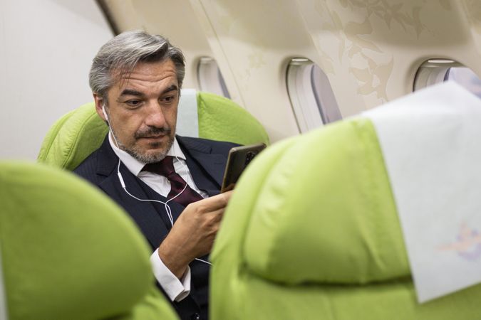Man using smart phone with ear buds in flight