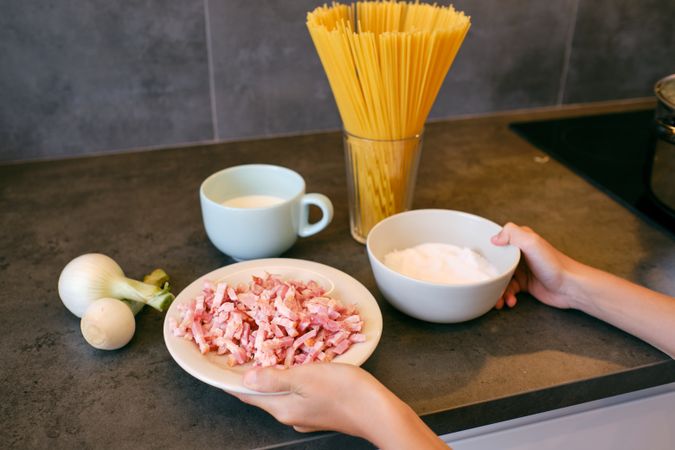 Crop person with cut bacon and salt cooking in kitchen