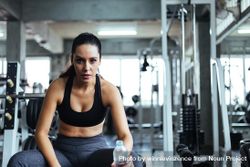 Woman sitting on bench in gym with water bottle 5zVZm5