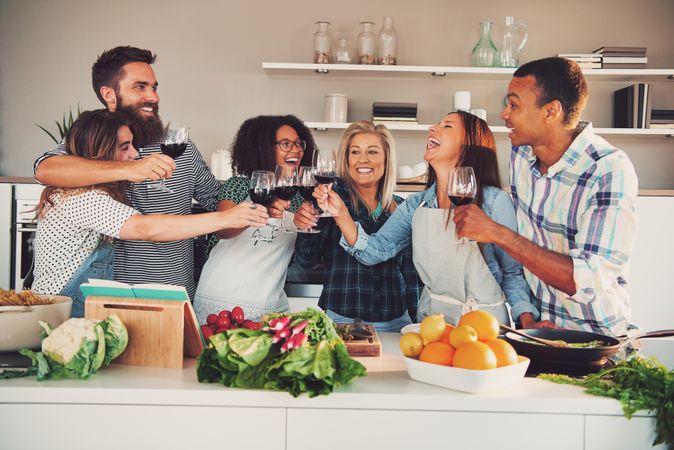 Group of friends toasting with red wine as they cook together at a dinner party