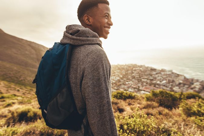 Cheerful man with backpack standing on mountain trail and looking away