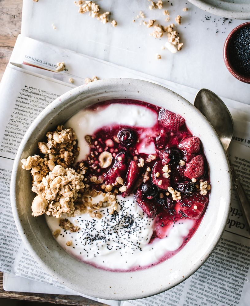 Delicious breakfast bowl with quinoa, rice and groats near tea cup and newspaper