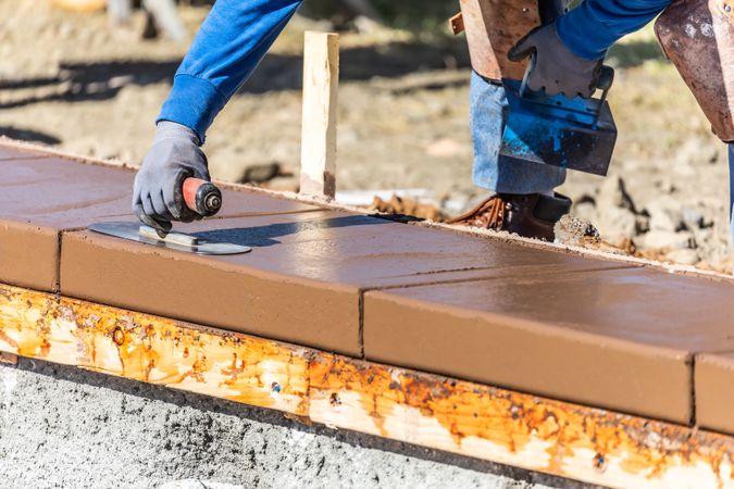 Construction Worker Using Trowel On Wet Cement Forming Coping Around New Pool