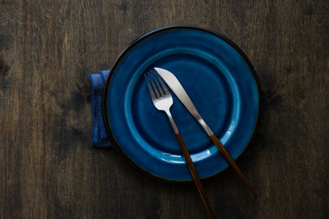 Blue plate on wooden table with cutlery