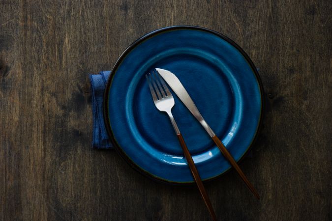 Blue plate on wooden table with cutlery