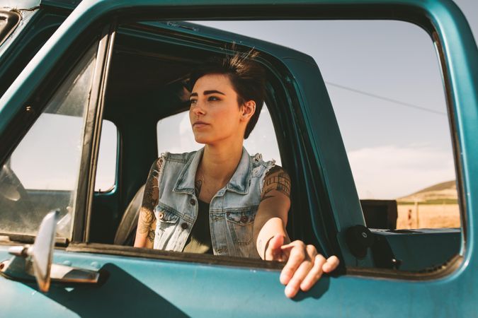 Woman with short hair and tattoos standing near open truck door looking out