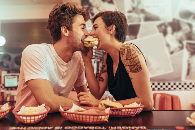 Happy couple at a restaurant eating a burger together looking at each other