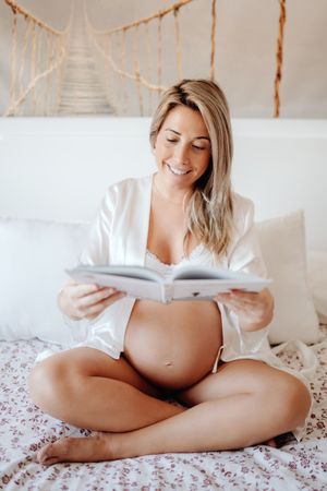 Smiling pregnant woman reading book at home